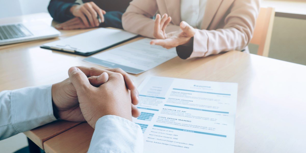 dois homens de terno conversando e um curriculo em cima da mesa
